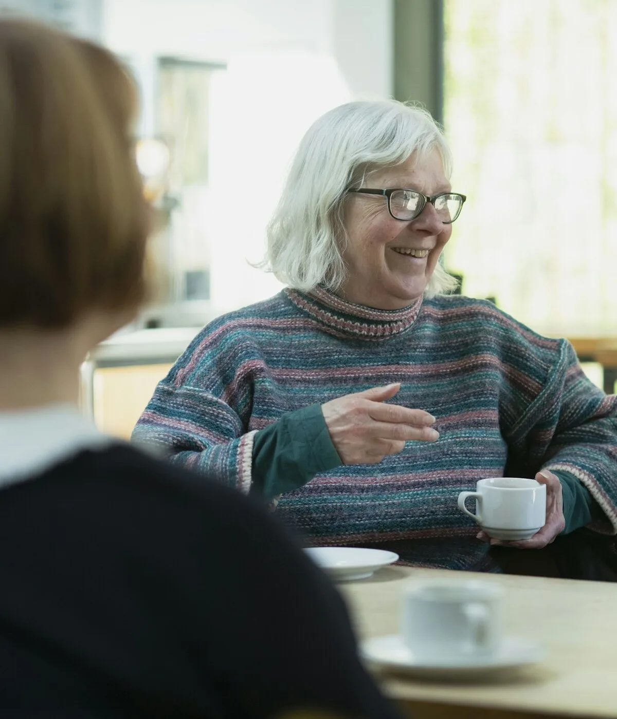 Ältere Dame im Gespräch bei einer Tasse Kaffee, zugewandt und lachend